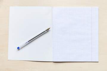 top view of pen and blank first page of open school notebook with squared sheets with margins on light brown wooden board