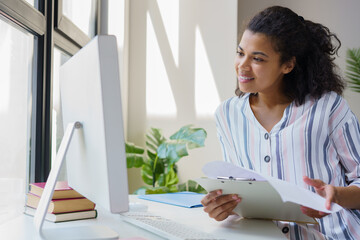 Portrait of beautiful African American businesswoman using pc computer holding documents sitting in office Smiling freelancer working at home 