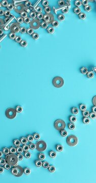 Vertical video, slow motion Male hand runs hand over Metal screw, nuts and bolts falling on blue background, Working tools, Fixing elements
