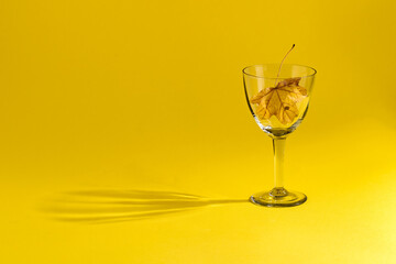 Concept - autumn in a glass. A glass with a yellow leaf on a yellow background. 