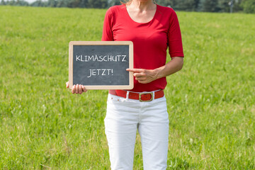 Frau auf einer Wiese mit einer Tafel Klimaschutz jetzt