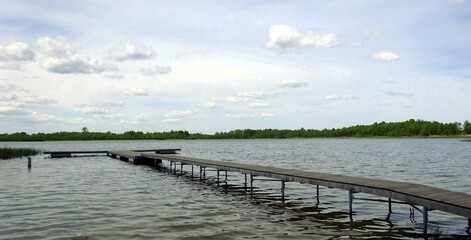 Fototapeta na wymiar Molo nad wodą z widokiem na jezioro oraz w oddali las.