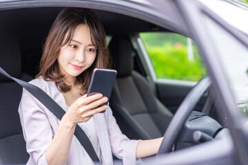 Fototapeta na wymiar スマホを使いながら車を運転する女性