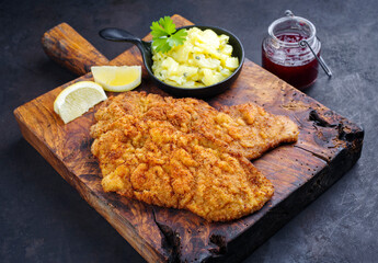 Traditionelles frittiertes Schnitzel mit Kartoffelsalat und Preiselbeeren serviert als close-up auf einem alten rustikalen Holz Board