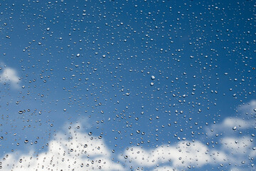 Raindrops on glass on a background of blue sky with clouds