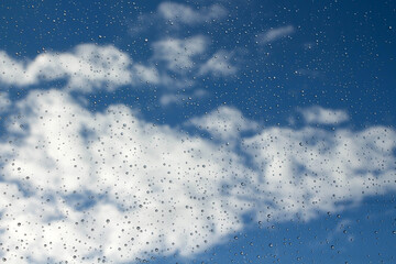 Raindrops on glass on a background of blue sky with clouds