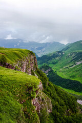Fototapeta na wymiar Kazbegi Mountains. View from the mountain to the city, the village of Stepantsminda. Green hills, mountain peaks. Travel in the mountains of Georgia.