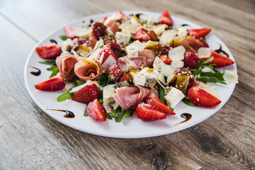salad with cheese. Diet summer strawberry salad with arugula. Fresh salad with arugula, strawberries, nuts and balsamic glasse sauce served on white plate on rustic wooden table. Healthy organic diet 