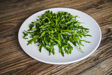 Obraz na płótnie Canvas Fresh arugula on a white plate on a wooden table background. Fresh salad for breakfast top view.