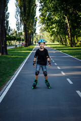 The boy is rollerblading on the track in the city park. The child learns to roller-skate. An active walk with a child on the street.