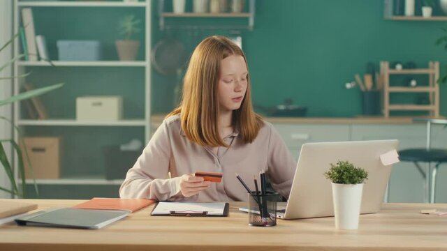 Happy Red-haired Teen Girl Shopping Online with a Card From Home. Consumer, Easy Shopping, Discounts, Online Shopping. Earlier Financial Development.