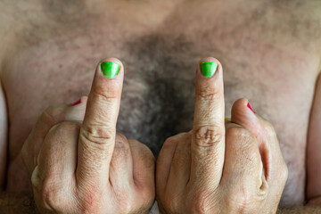 Close-up with selective focus of male fingers with green painted nails doing the sign to fuck off.