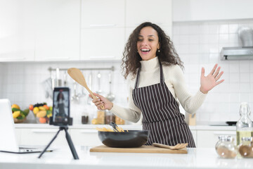 Latin women live streaming online with a smartphone while cooking in the kitchen at home.