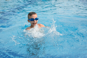 Fototapeta na wymiar boy swimming in the pool. Boy in blue goggles for swimming in the pool. Summer vacation of a child in the pool.