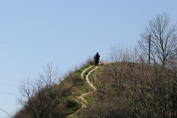 Early spring, a man climbs to the top of a hill along a winding path.