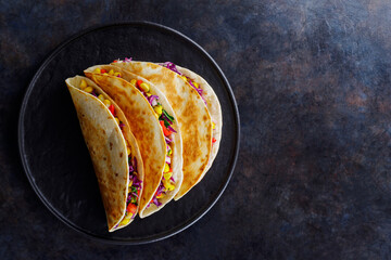 Vegetarian tacos with sweet corn, purple cabbage and tomatoes on a black plate. Tacos with vegetables and guacamole sauce on dark background. Copy space. Top view