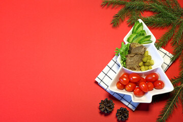 Holiday snack on Christmas tree plate on red background. Top view.Space for text.