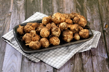 Raw Jerusalem artichoke in a clay bowl on wooden boards background. Raw Organic topinambour