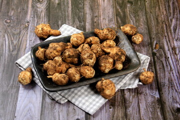 Raw Jerusalem artichoke in a clay bowl on wooden boards background. Raw Organic topinambour