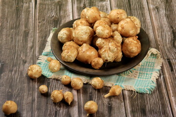 Raw Jerusalem artichoke in a clay bowl on wooden boards background. Raw Organic topinambour