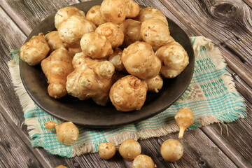 Raw Jerusalem artichoke in a clay bowl on wooden boards background. Raw Organic topinambour
