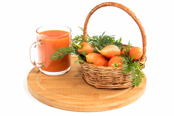 On a wooden cutting board, a wicker basket with fresh carrots and healthy rich carrot juice in a glass. 