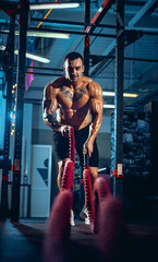 Front view of young man, muscled athlete, bodybuilder training alone at sport gym, indoors. Concept...