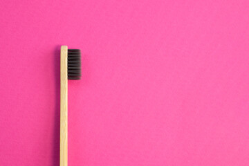 Wooden bamboo toothbrush with black bristles. Natural eco friendly zero waste item on pink background