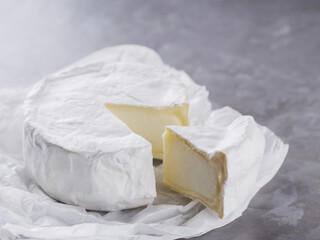 Camembert on a gray cement background. Soft cheese with white mold on parchment paper. Copy space. Top view