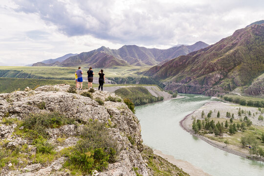 A family admires mountain river while standing on high steep bank at the confluence of the Katun and Chuya rivers in the Altai Republic