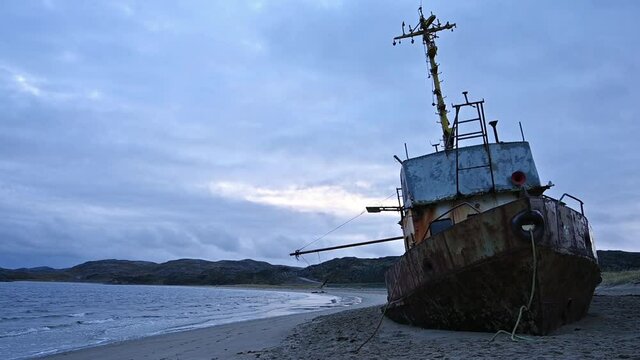 An old rusty longboat on the shore of the Barents Sea against the background of a dramatic sky at sunset. Russian North Teriberka village
