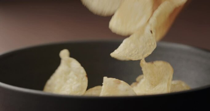 Slow motion potato chips fall in black bowl closeup