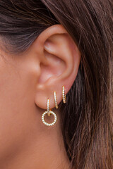 Woman ear with mulriple piercings wearing beautiful earrings with zirconia - obrazy, fototapety, plakaty