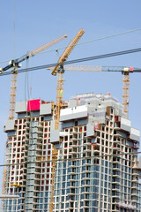 Large residential tower under construction with three yellow large cranes on top in The Hague in the Netherlands
