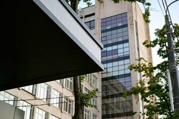 Detail of the building. Stop. Foreground. Background. University building. Leaves of trees. Green color. Window