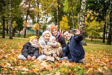 Happy mom, dad and sons playing having fun together, taking selfie on the mobile phone at the autumn park.