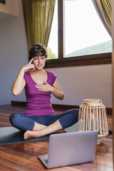 Young meditation teacher teaching pranayama breathing from her computer at home.