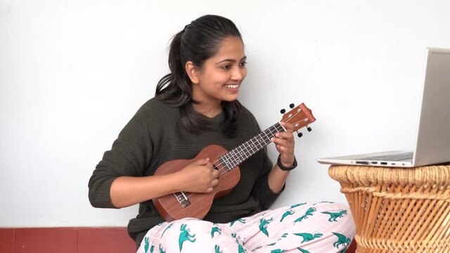 Young woman playing ukulele in front of a laptop. Concept of online learning and teaching	