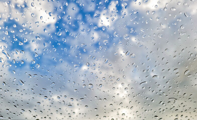 Raindrops on glass window with blue sky and white cloud background