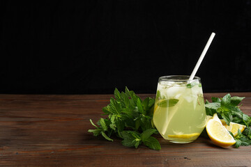 Lemonade or mojito cocktail with lemon and mint, cold refreshing drink or beverage with ice on rustic wood background. Homemade lemon and ginger organic drink, copy space.