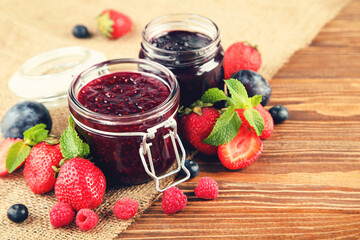 Sweet jam in glass jars with ripe berries on brown wooden table