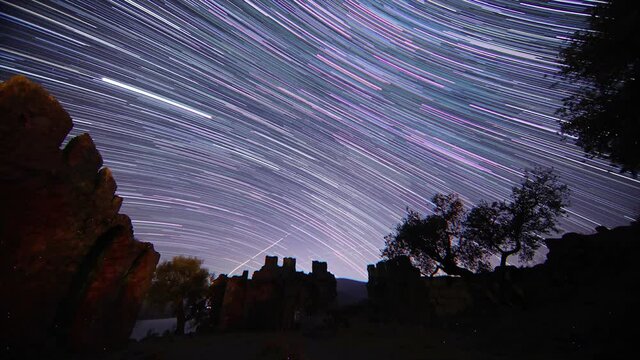 old castle in the night. Timelapse of moving star trails in night sky. A view of the stars of the Milky Way with a mountain top in the foreground. Perseid Meteor Shower observation.