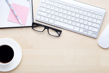Computer keyboard with notepad, glasses and cup of coffee on wooden table