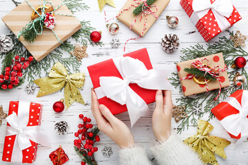 Female hands holding gift box with christmas ornaments on white wooden background