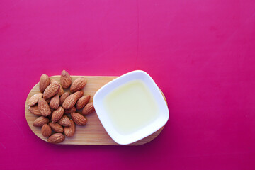Almond oil in a container and almond nut on color background. 