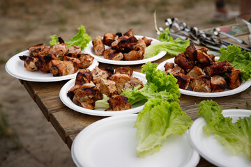 Ready-made delicious meat shish kebab cooked over coals over a fire. Pieces of meat fried on the grill. City food festival, food court, street food. Cooked meat in plates with lettuce leaves.