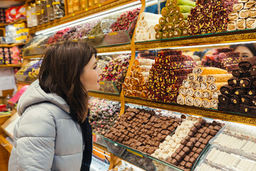Young woman looking at Turkish delight, various lokum, colorful sweets and chocolate at store selling delight