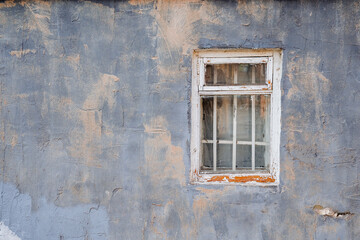 Old window with a wooden frame and a lattice in a purple wall with beige spots. Peeled white paint on the frame.