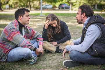 Naklejka na ściany i meble Three friends sit together in park and talk about problems