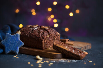 Homemade gluten free vegan chocolate banana bread with cinnamon sliced and serves on a wooden cutting board with holiday decorations and bokeh on a dark purple moody background